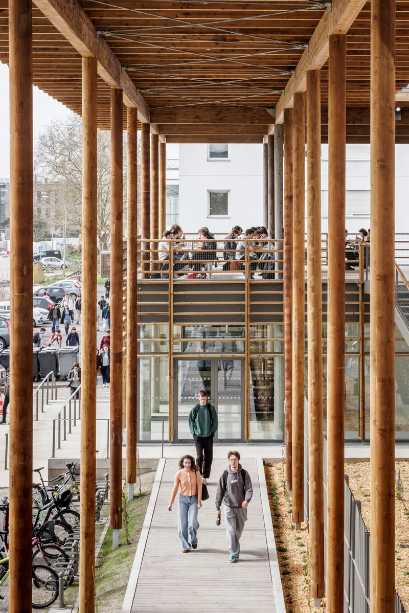 View through timber columns to the lower promenade with two people walking beneath exposed roof beams
