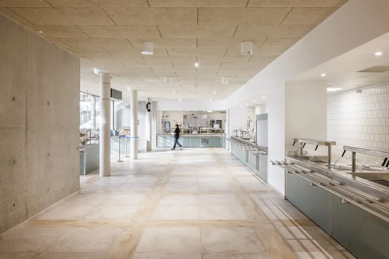 Corridor with concrete columns and light-toned flooring leading past service counters and a figure in motion