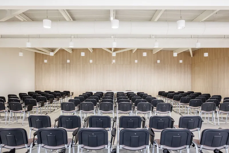 Assembly hall with rows of black chairs facing a vertical timber-clad wall under exposed white trusses