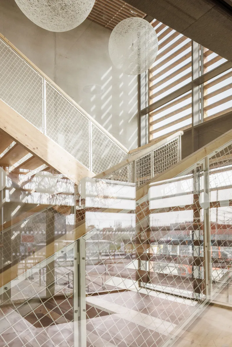Stairwell with wire mesh balustrades and timber louvers casting diagonal shadow patterns across white walls