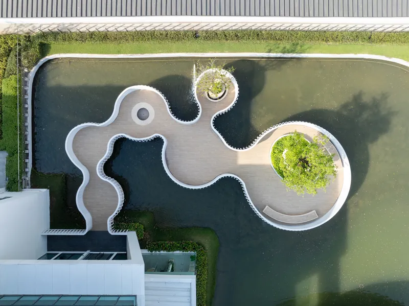 Aerial view of the sinuous white boardwalk deck winding through dark pond water with planted islands