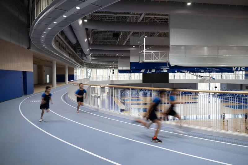 Indoor running track with students in motion under curved ceiling panels and exposed mechanical systems