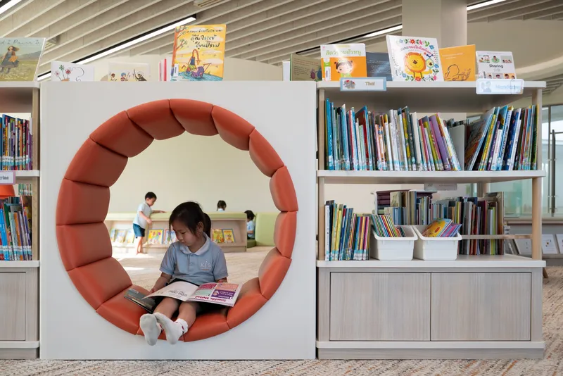 Circular padded reading nook set into white bookshelf partition with child seated inside holding a book