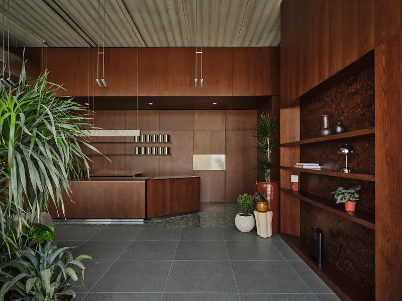Reception desk with walnut cabinetry and cork-backed shelving adjacent to potted plants