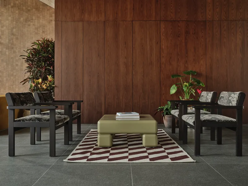 Seating arrangement with black timber chairs and pale ottoman on geometric rug against wood paneling