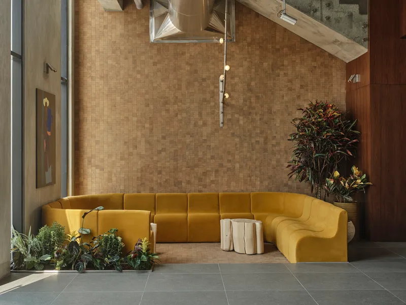 Corner view of the yellow sectional seating beneath suspended light fixture and exposed ceiling ducts