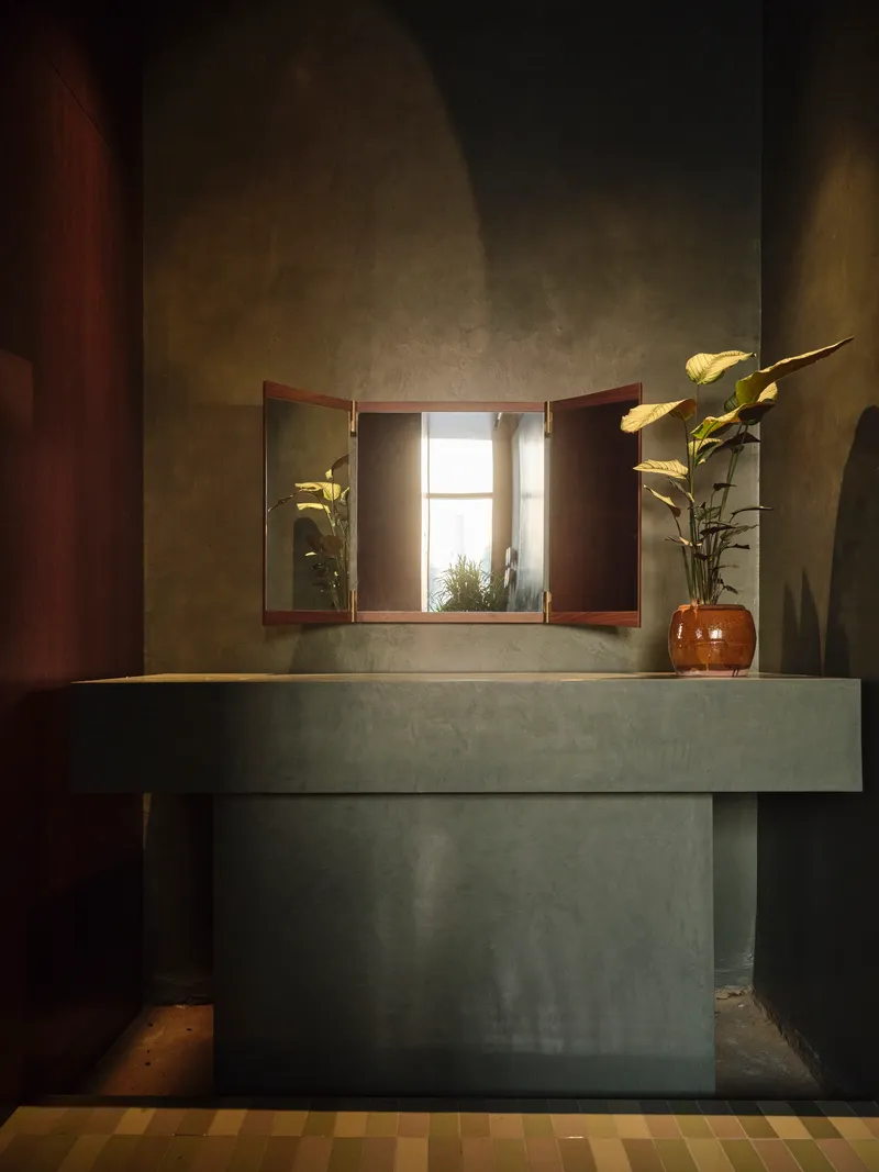 Concrete vanity unit with triptych mirror reflecting a window in a dimly lit washroom