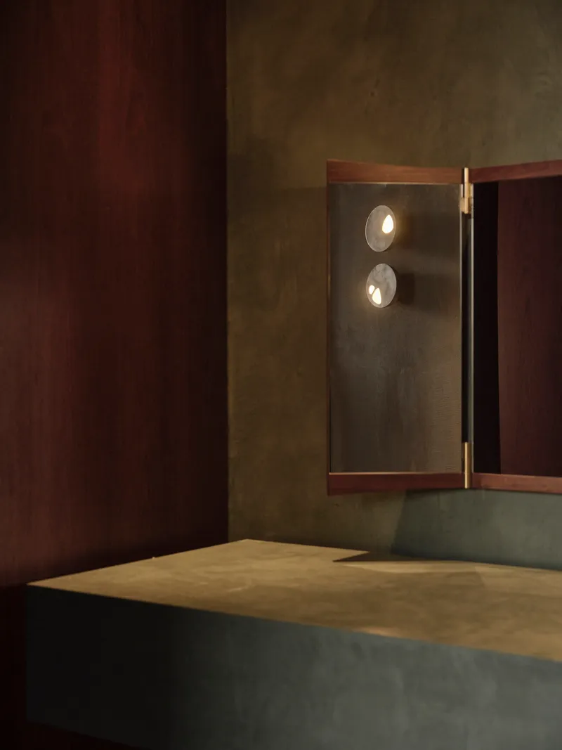 Illuminated triptych mirror panel with brass hinges set into dark timber and concrete walls