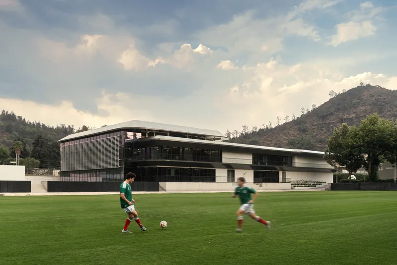 Long view of the louvered facade and sweeping roofline from the playing field with two players in motion
