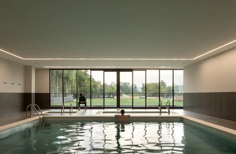 Indoor pool with full-height glazing overlooking the sports field and dark tile wainscoting