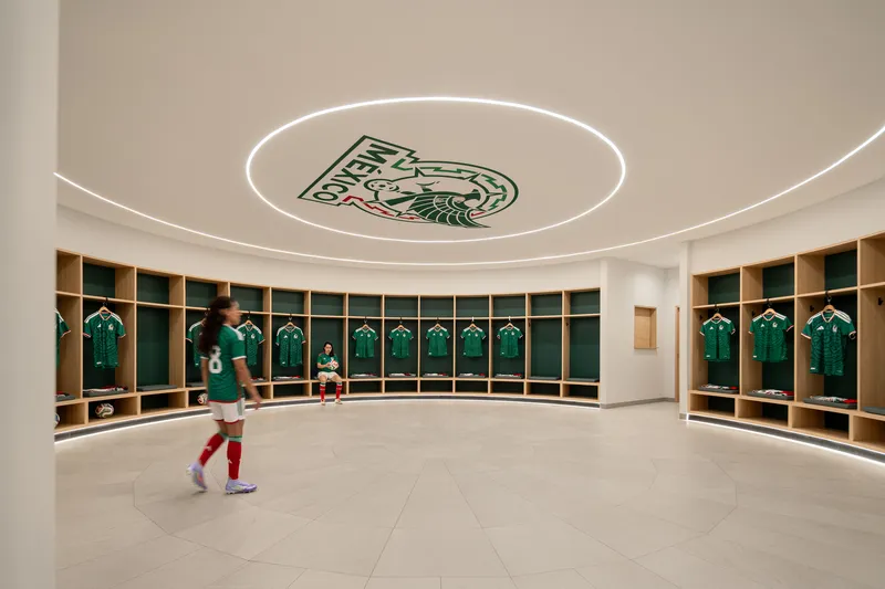 Circular locker room with curved timber benches, green jersey cubbies and illuminated ceiling emblem