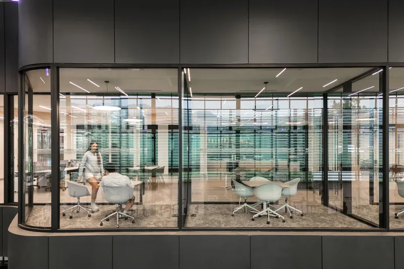 Curved glass-walled conference room with white task chairs and a figure moving past the glazed enclosure