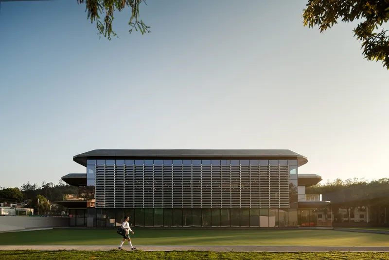 Horizontal louver facade wrapping the street elevation as a figure crosses the lawn at dusk
