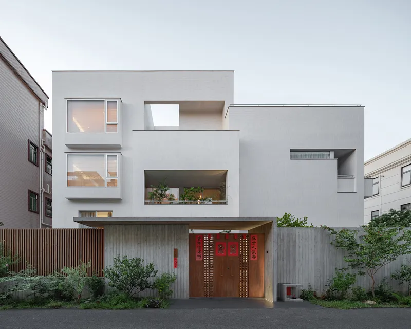 Street view showing the layered white volumes with recessed balconies and timber entry gate