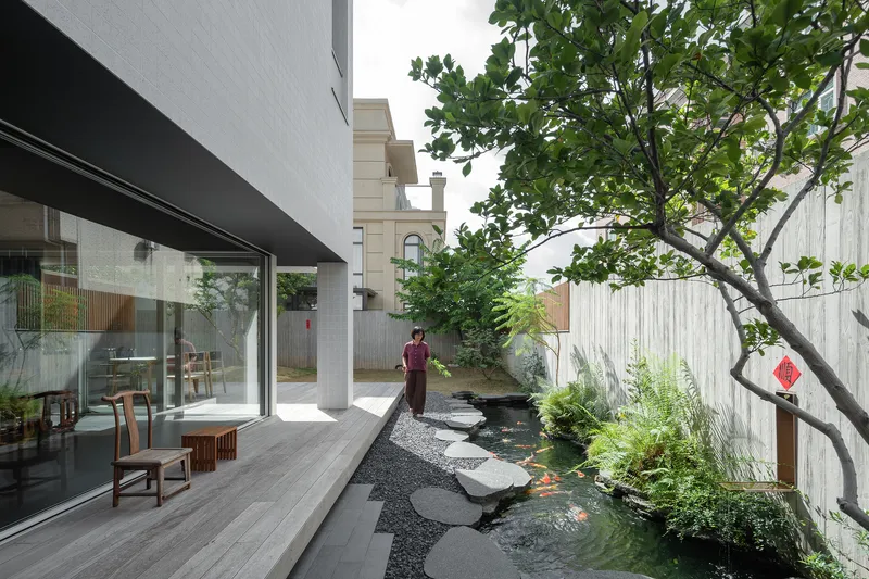 Courtyard with stepping stone path through koi pond alongside glazed living room and mature tree
