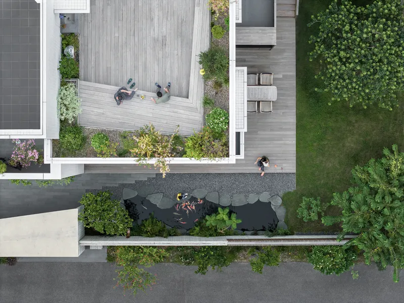 Aerial view of timber decks, koi pond with residents, and planted beds between house volumes