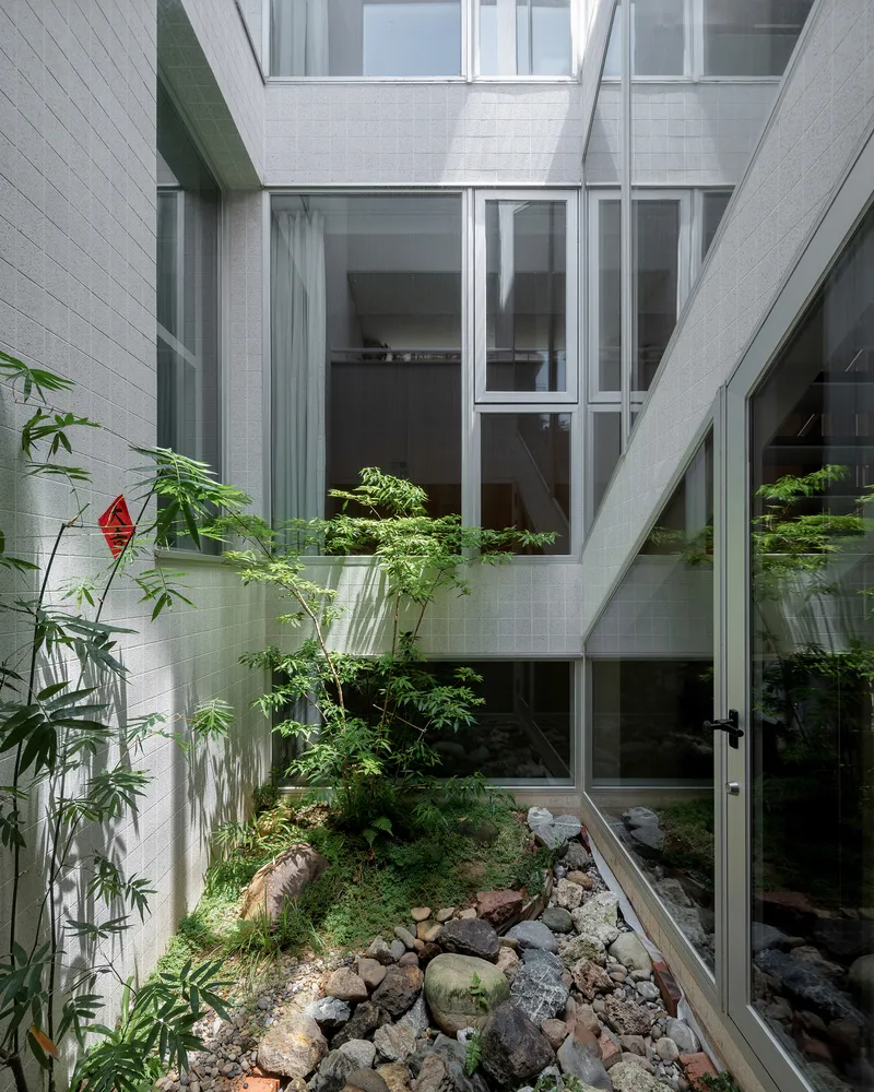 Interior courtyard with white tile walls, layered glazing, bamboo, and rock garden below