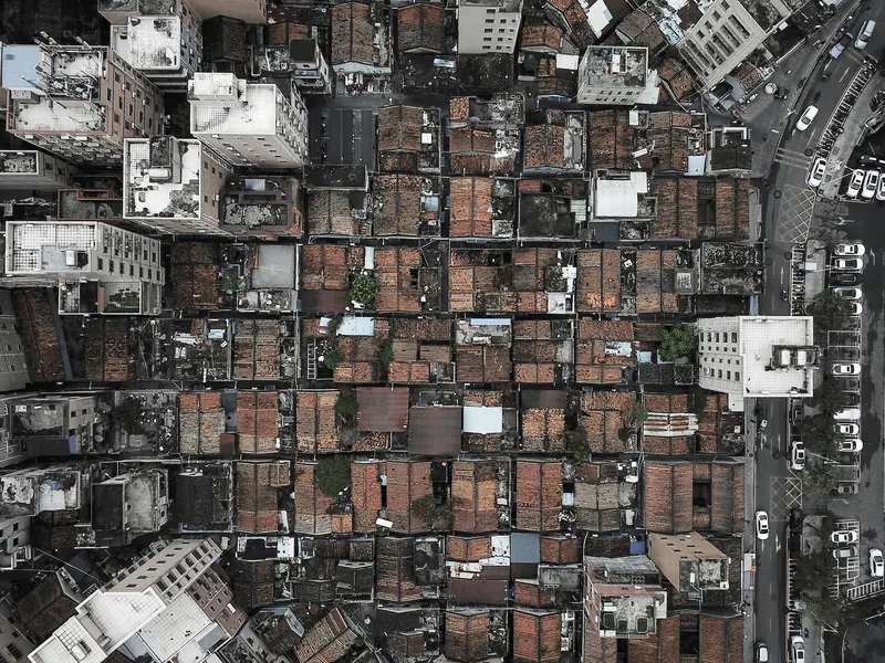 Aerial view of densely packed rooftops with varied tile colors and scattered vegetation between buildings