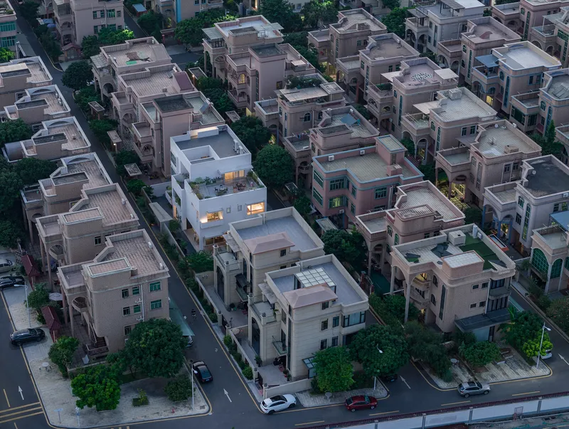 Drone view of residential blocks at dusk showing a white multi-level house among pink-toned neighbors