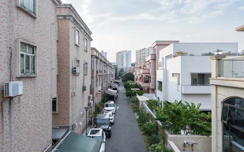 Street view between brick residential blocks with parked cars and green landscaping under cloudy skies