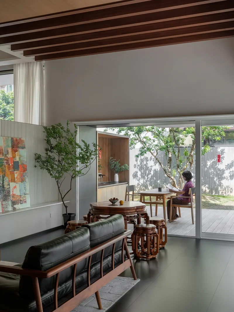 Living room with exposed timber ceiling beams opening to a courtyard where a person sits at a table
