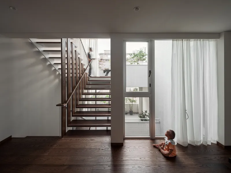 Open-tread timber staircase rising through a room where a child sits near glazed doors