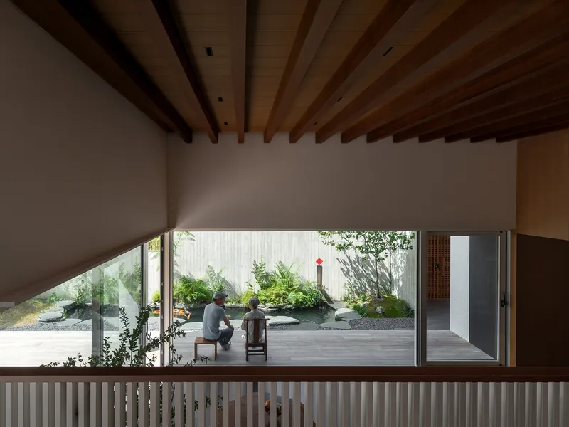 View from upper level through slatted balustrade toward seated figures beside a planted courtyard