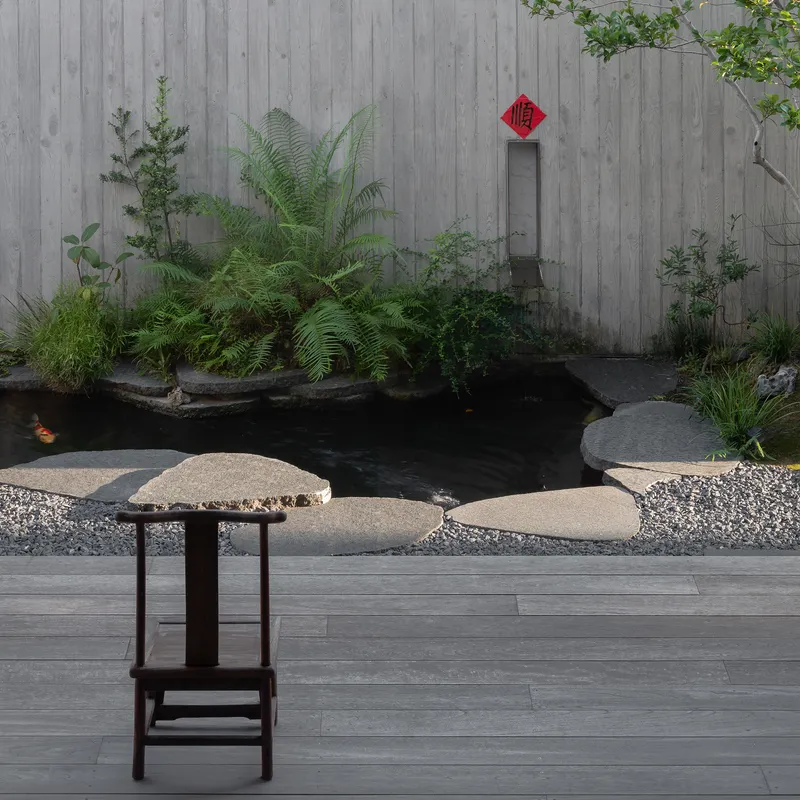 Courtyard pond with stepping stones and ferns against a vertical timber board wall