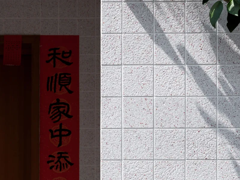 White textured tile wall with dappled shadows from a tree beside a red scroll