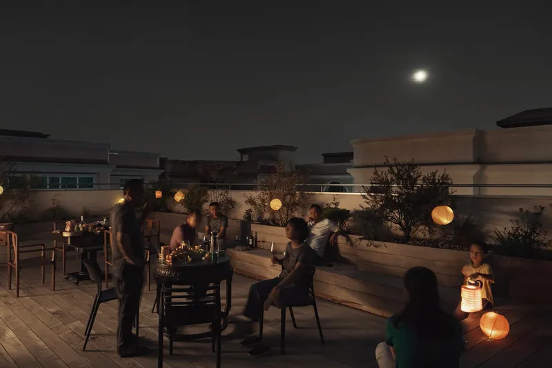 Rooftop terrace with timber benches and globe lighting where families gather at dusk under a full moon
