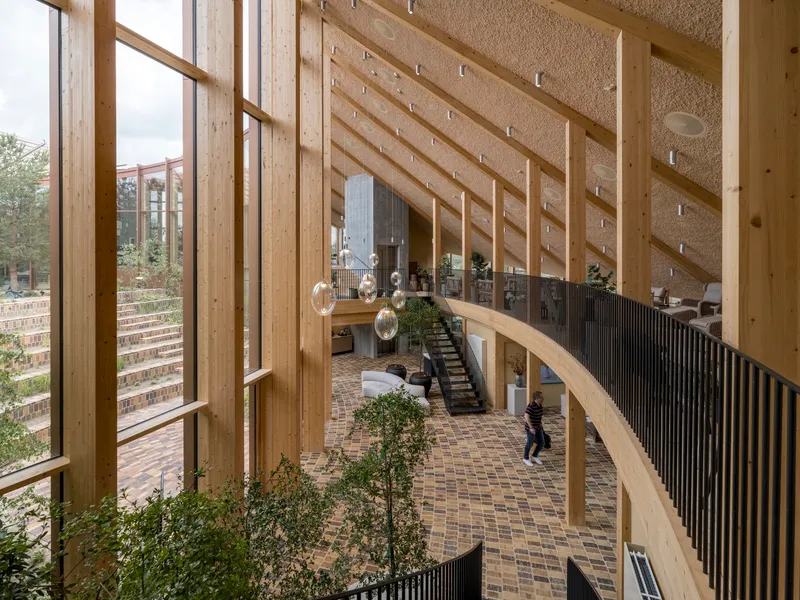 View from upper level walkway showing curved timber balustrade and patterned brick floor with visitors below