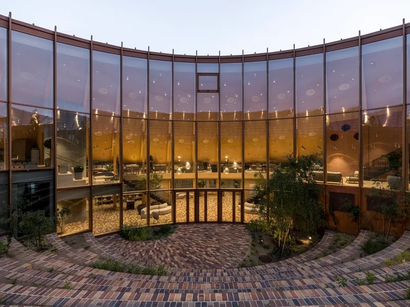 Interior courtyard enclosed by curved glass walls with timber mullions illuminated at twilight