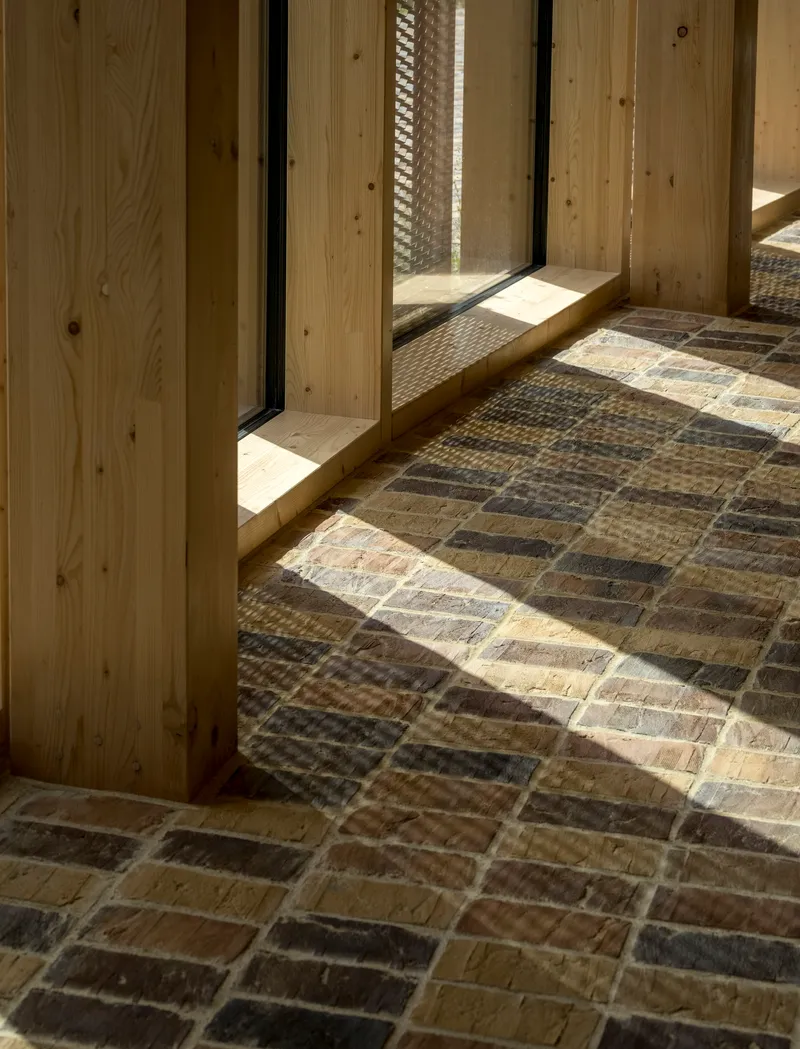 Sunlight casting shadows across multicolored brick floor at timber door threshold with mesh screen beyond