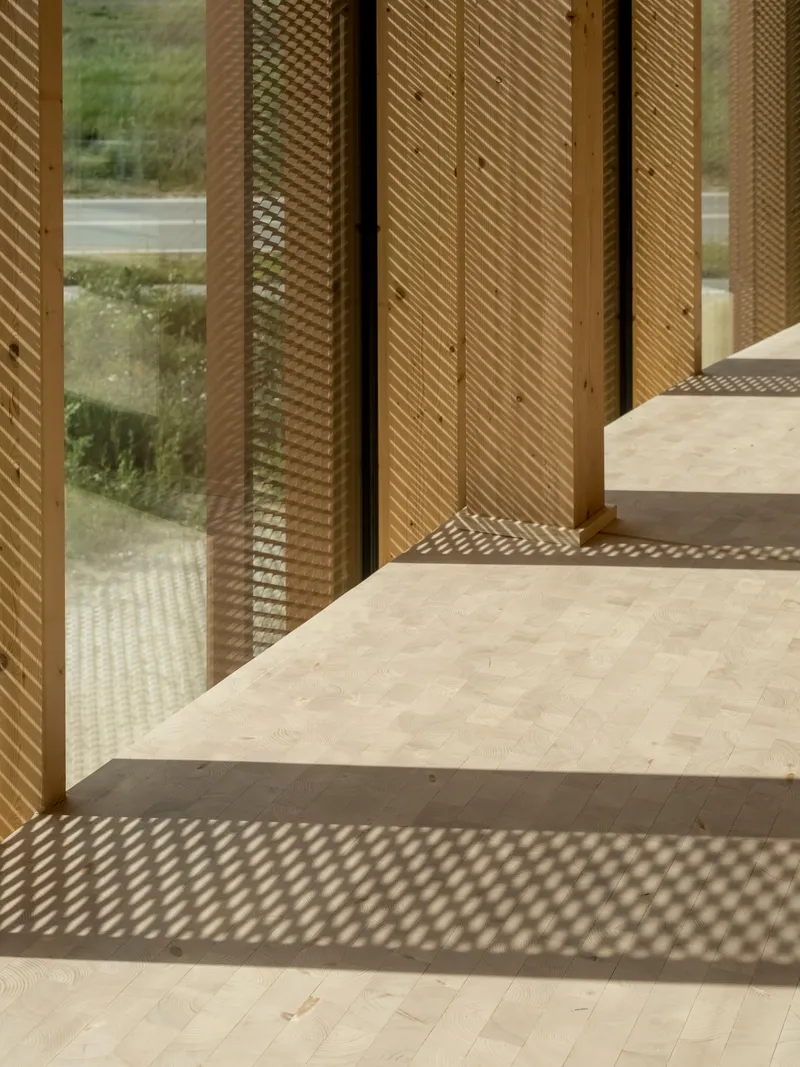 Perforated metal screen panels and timber frame casting latticed shadows on pale timber floor