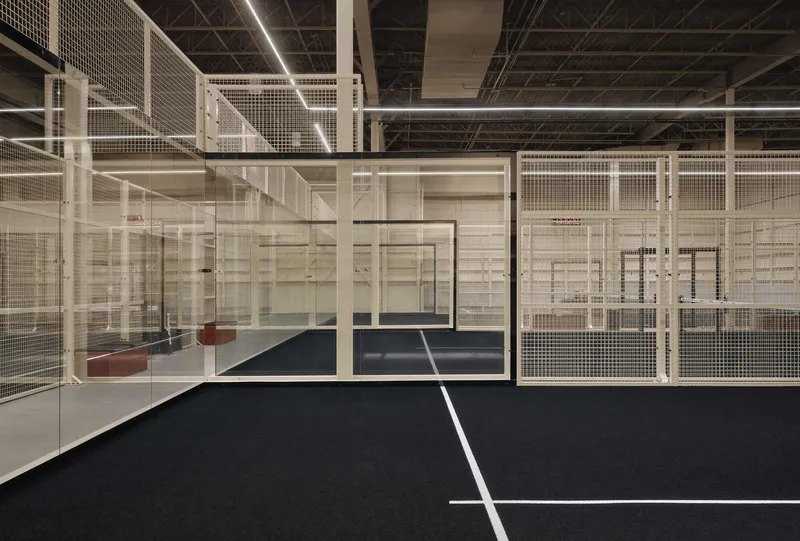 Indoor sports court enclosed by white metal mesh partitions beneath an exposed joist ceiling with linear lighting
