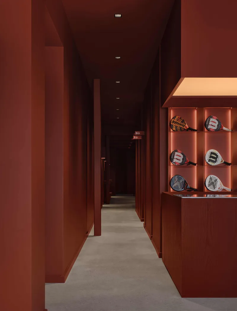 Narrow corridor with terracotta-paneled walls, concrete flooring, and display niches containing sports equipment