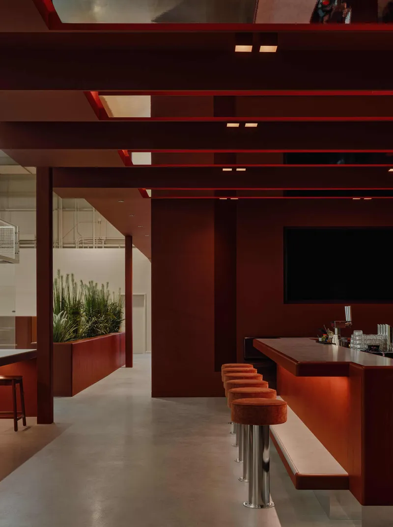 Interior bar area with horizontal terracotta beams, integrated uplighting, and planted planter box dividing spaces