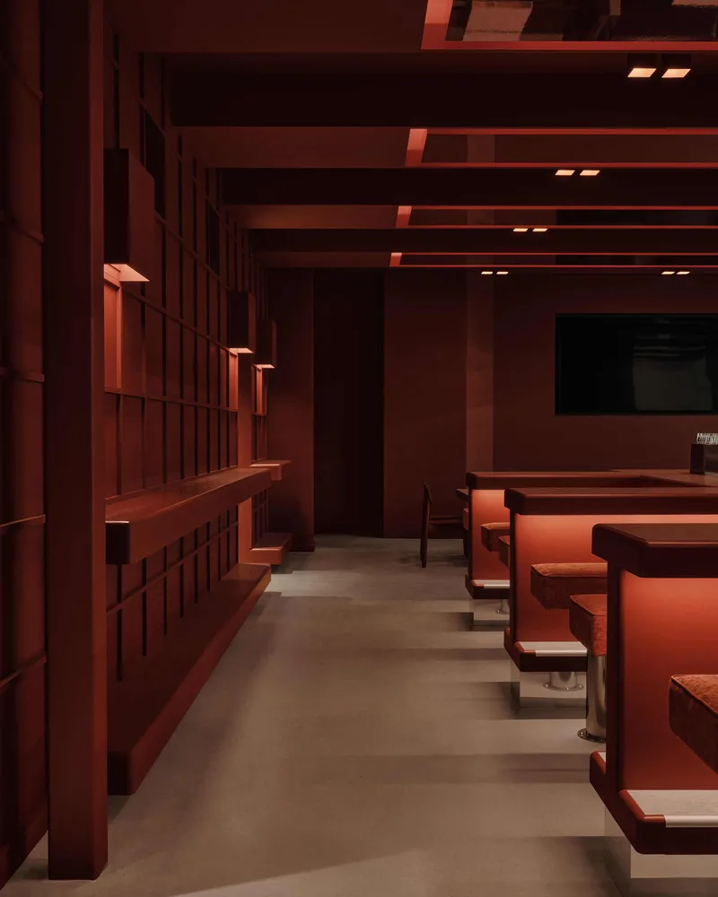 Seating area with gridded storage wall, horizontal beam ceiling system, and concrete floor under warm lighting