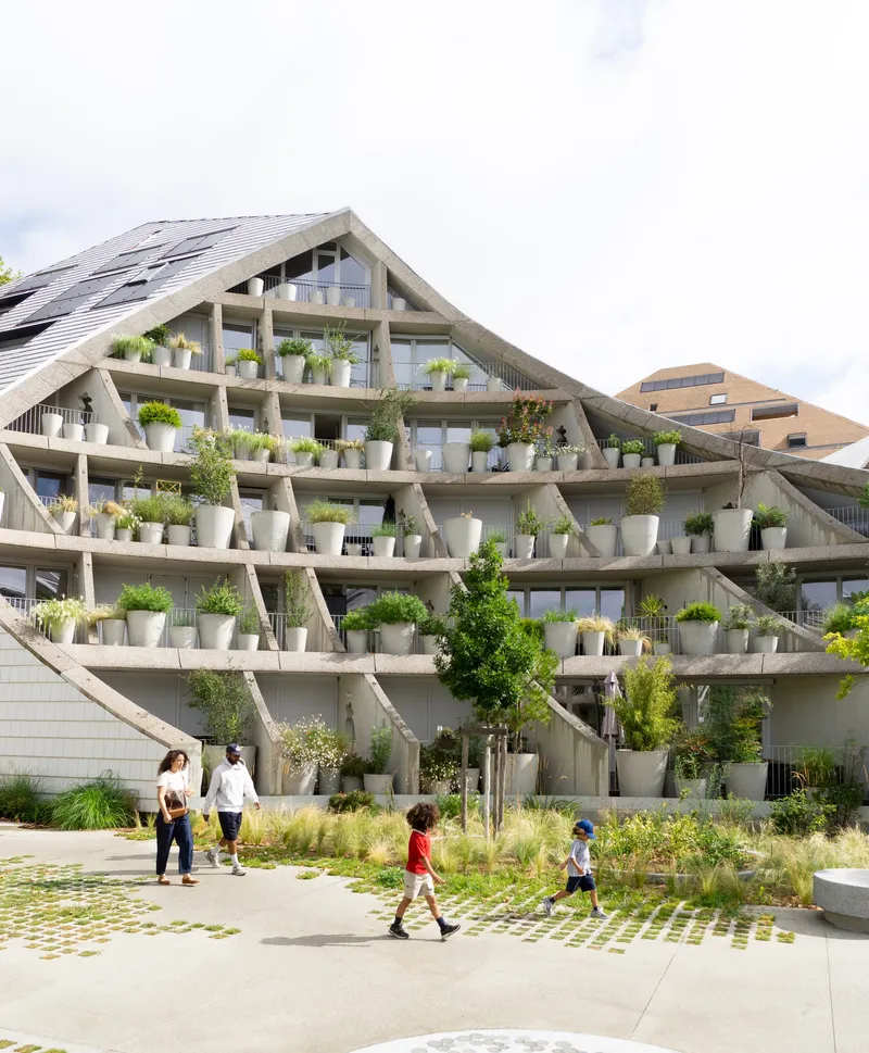 Gabled facade with exposed concrete diagonals and planted terraces as families walk through courtyard