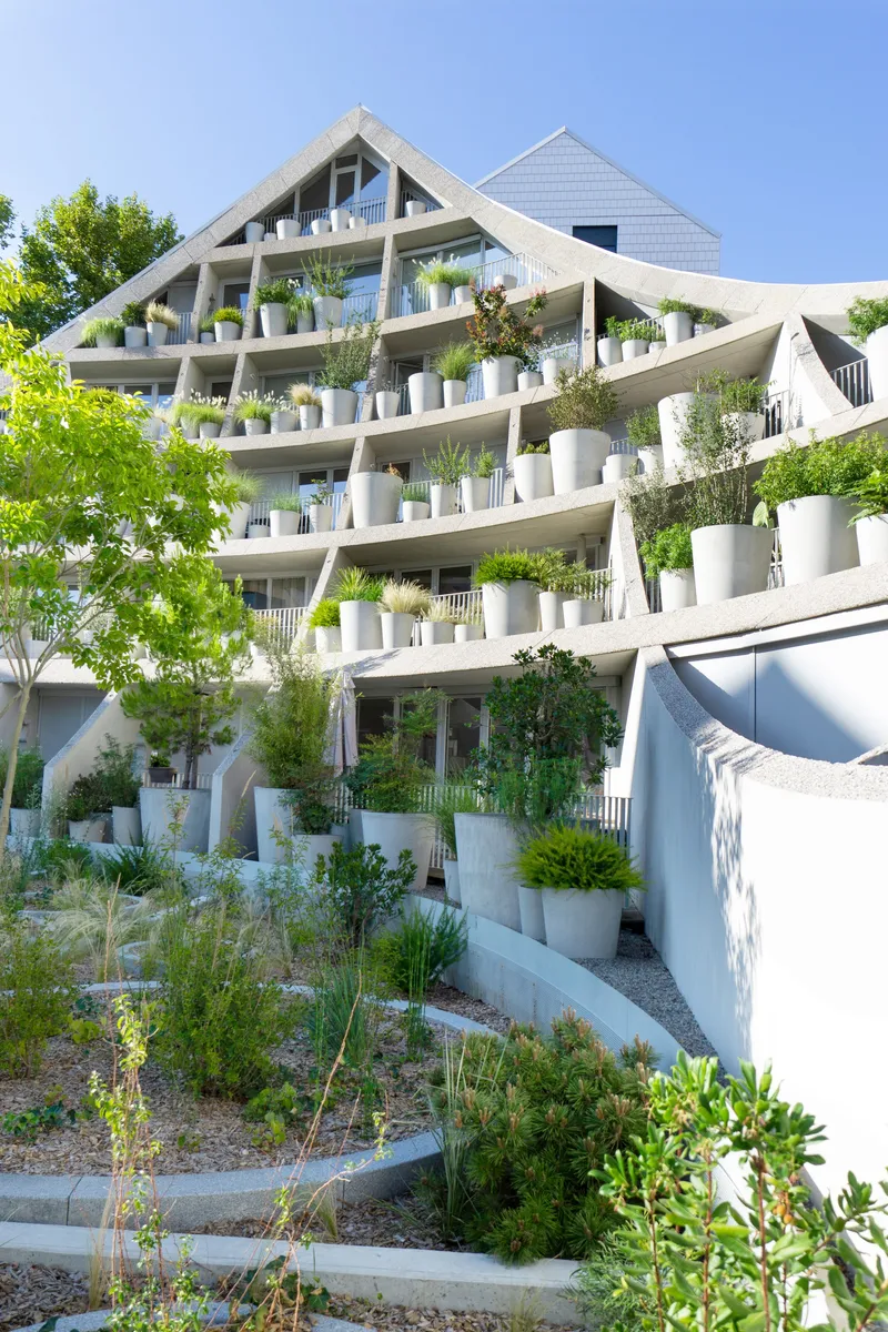 Ground-level view of the planted terraces with diagonal concrete beams and white cladding above
