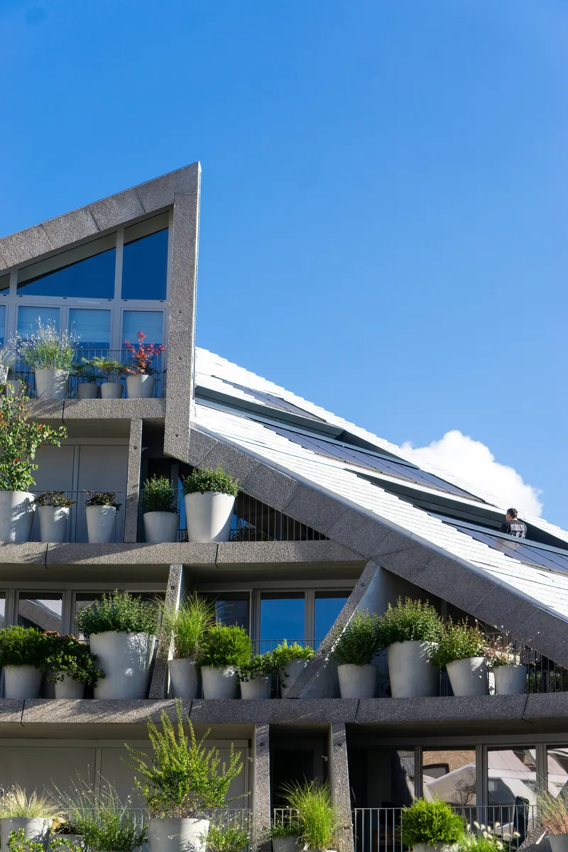 Stepped balconies with white planters and solar panels on the sloped roof against a clear blue sky