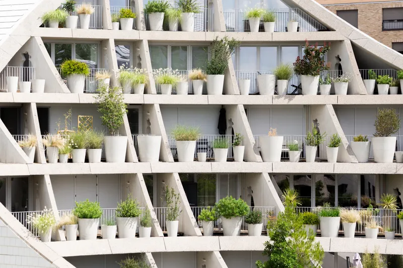 Close-up of diagonal concrete beams supporting stepped balconies lined with white potted plants