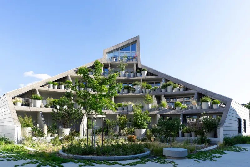 Angled facade with planted terraces surrounding a paved courtyard with grid pattern and small trees