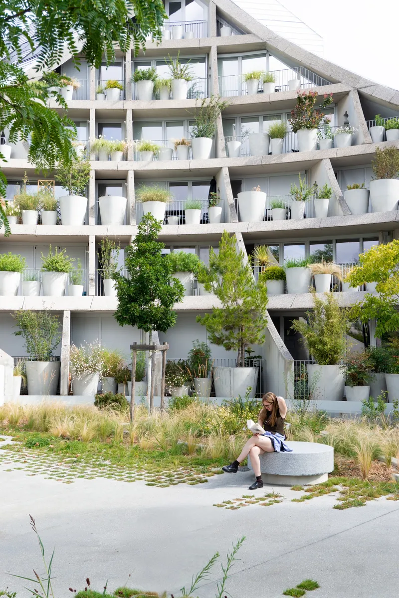 Concrete terraces with white planters and trees as a person sits on a stone bench in the foreground