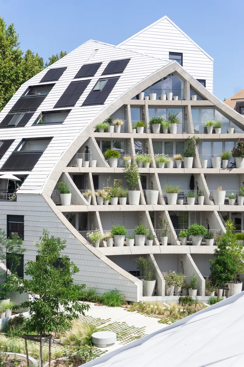 Triangular exoskeleton facade with planted balconies and white cladding under a clear summer sky