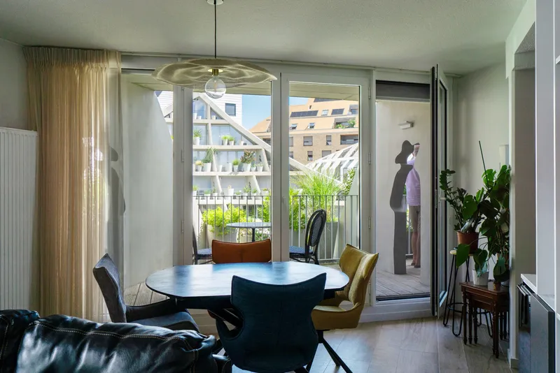Dining area with round table, glass doors opening to planted balcony, and sheer curtains filtering light
