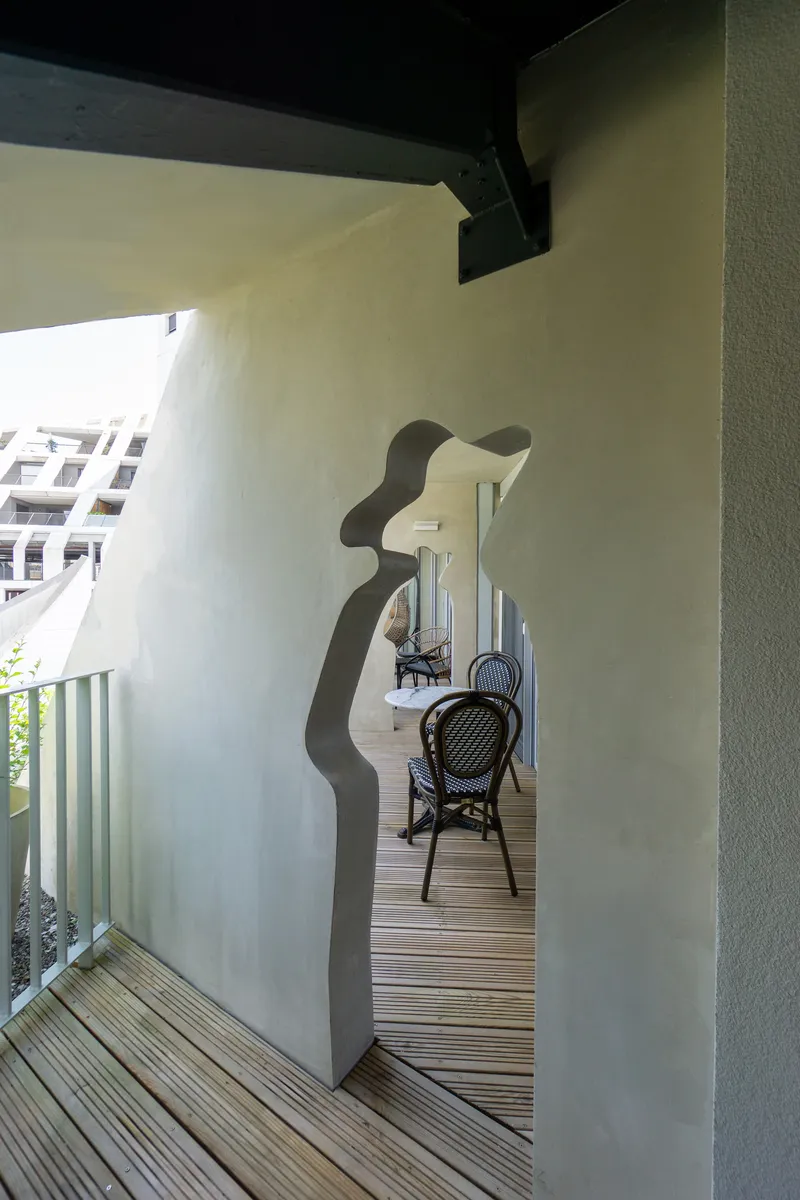 Terrace with organic-shaped portal opening in a pale plaster wall leading to a seating area with timber decking
