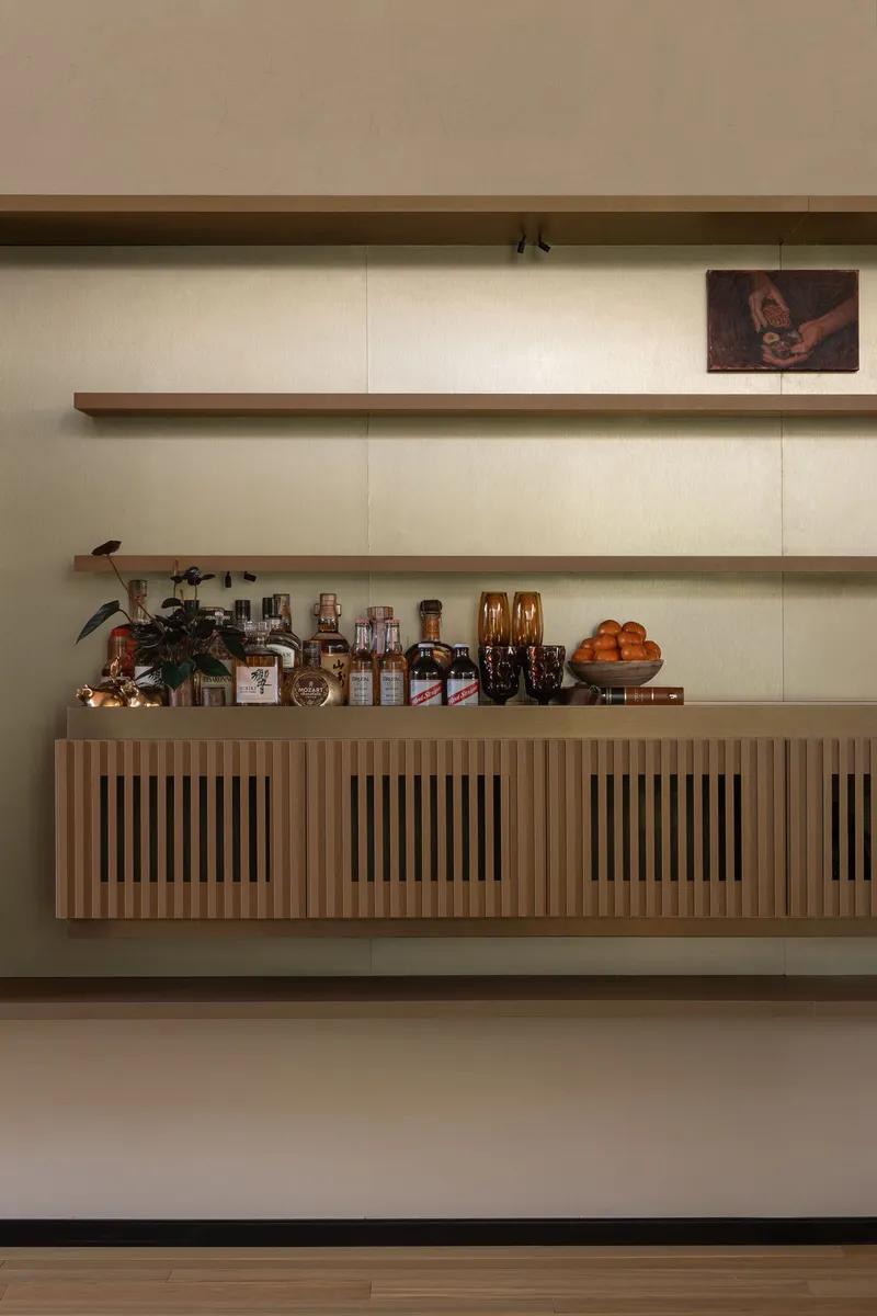 Built-in credenza with vertical slat panels and timber shelves displaying bottles and objects