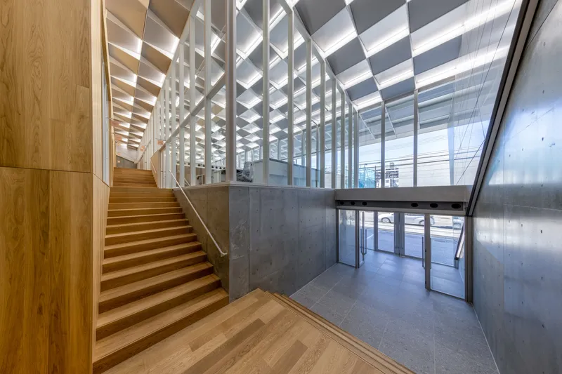 Timber staircase ascending from entry lobby with geometric ceiling coffers and concrete walls