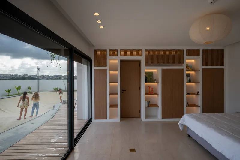 Bedroom with built-in timber storage wall and glass doors opening to wooden deck at dusk